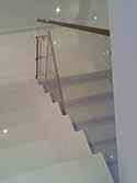 Elementy zabezpieczajace ze stali nierdzewnej montowane na balustradzie szklanej na klatce schodowej